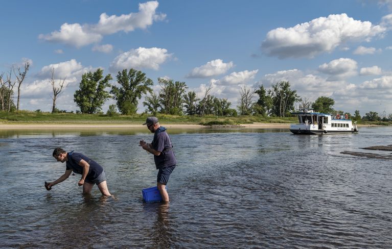 [Translate to English:] Zwei M&auml;nner stehen in der Elbe und nehmen Proben. Im Hintergrund sieht man das Forschungsschiff ALBIS.